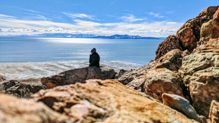 man in black jacket sitting on rock near sea during daytime