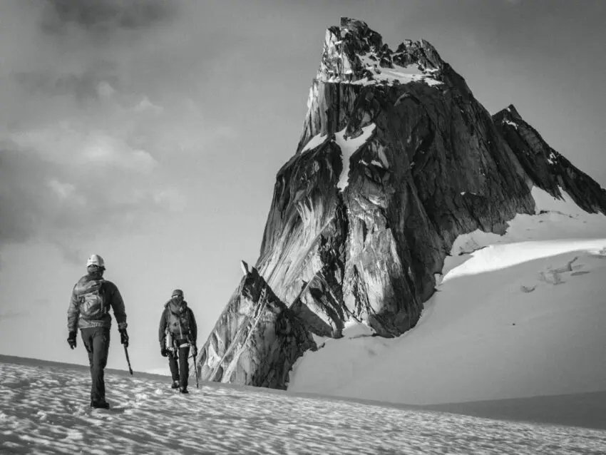 grayscale photo of two people walking on mountain valley
